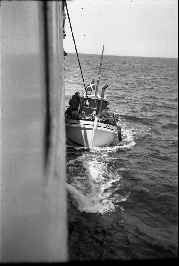Den lille passager- og postbåd KJELDSEN, der i januar 1952 blev taget i brug til at betjene Tunø. Fra juni 1965 blev den reservebåd og endeligt frasolgt i 1976. Billedet viser KJELDSEN, der går på siden af et af DSBs passagerskibe KALUNDBORG eller JYLLAND i 1955 for at post, gods og passagerer fra/til Tunø kan overføres, mens DSB-skibet er sagtet ned på rejsen mellem Kalundborg og Aarhus (via Kolby Kås) eller omvendt. Foto: Evald Jensen